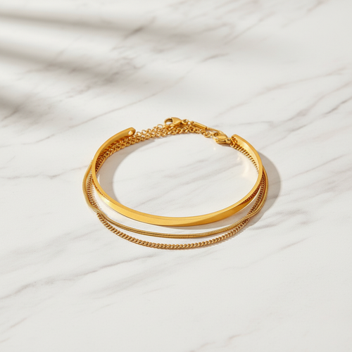 Gold cuff bangle and chain bracelet set on white marble